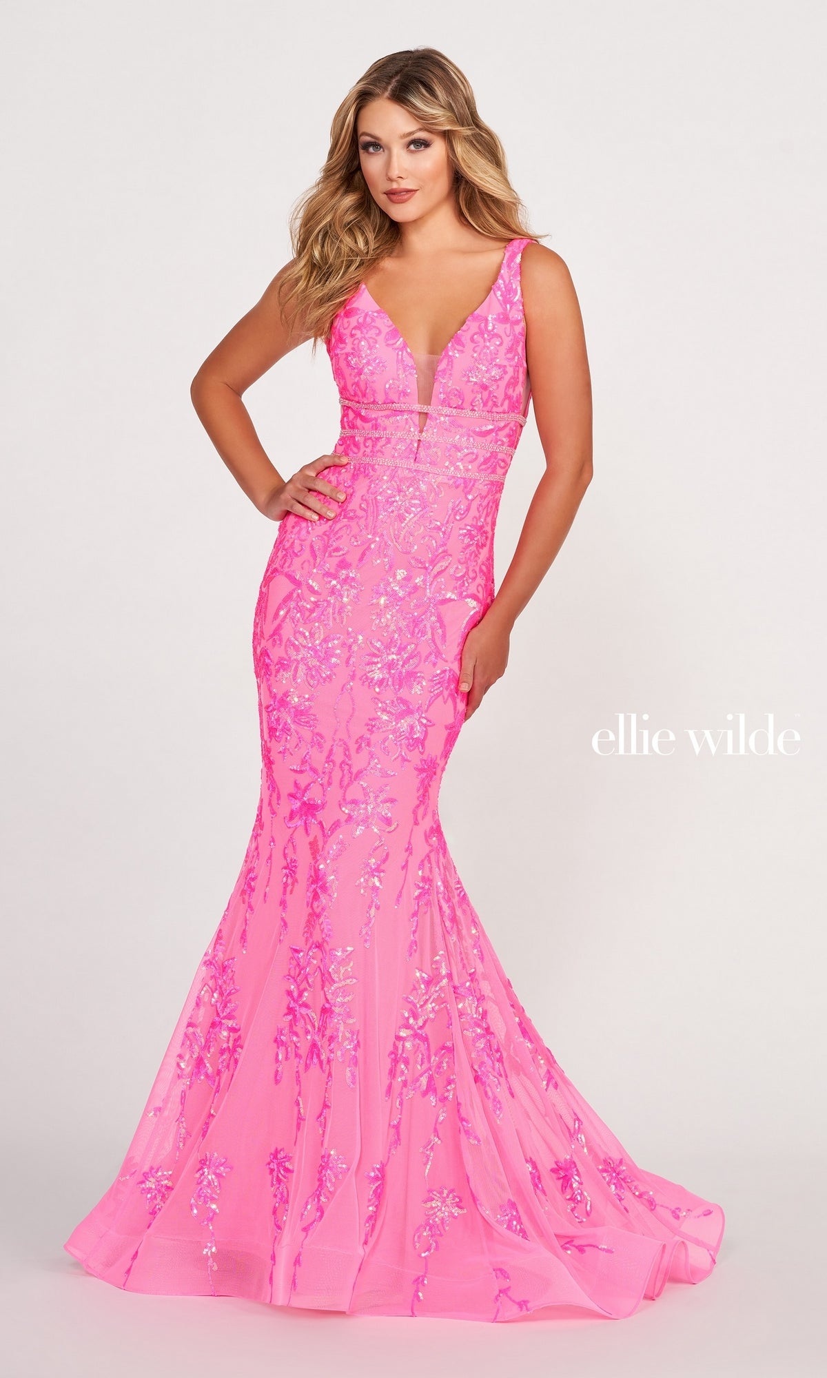 A woman wears the Banded-Waist Long Sequin Mermaid Prom Dress, a fitted bright pink gown with floral patterns, a deep V-neckline, and a floor-length sequin mermaid skirt for an elegant look.